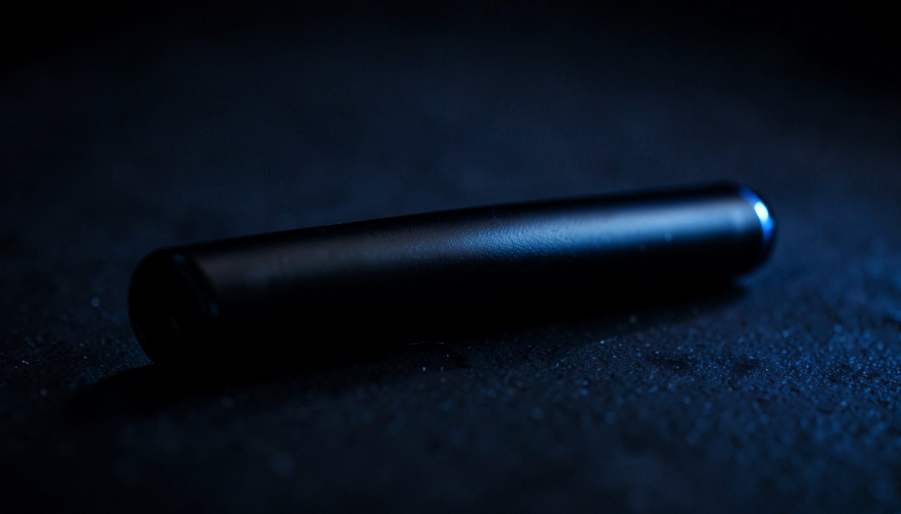 Dark atmospheric close-up of a sleek disposable vape pen with a matte black finish, resting on a shadowy surface